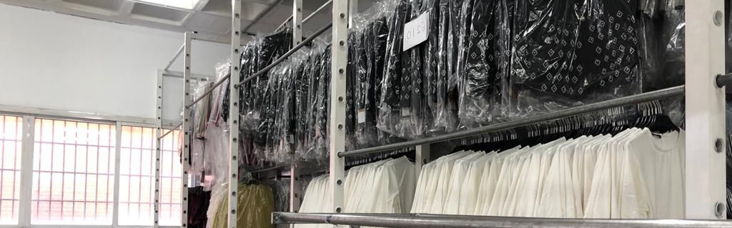 Interior del taller de Needle Textil: prendas confeccionadas y en proceso, colgadas y protegidas, junto a la mesa de corte